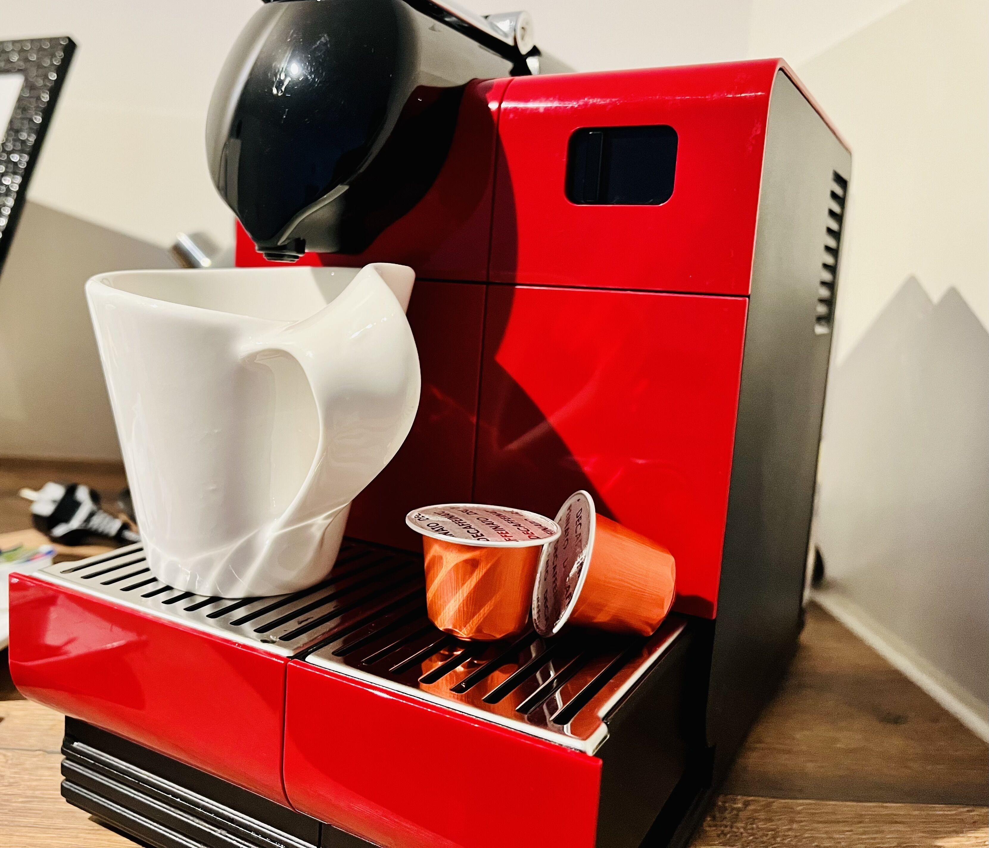 Een rode espressomachine met een witte bekerhouder en twee koffiecups.