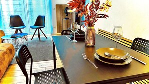 A dining area with a dark wooden table, black chairs, a vase with flowers, and a wine glass. - Nivas - 2 rooms, kitchen, bathroom, 6 persons (Montabaur)