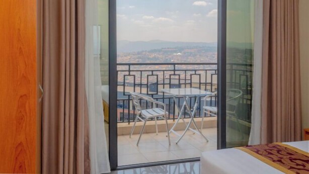 A room with a balcony, a bed, and a view of the cityscape. - Tropical Plaza Apartments (Kigali)