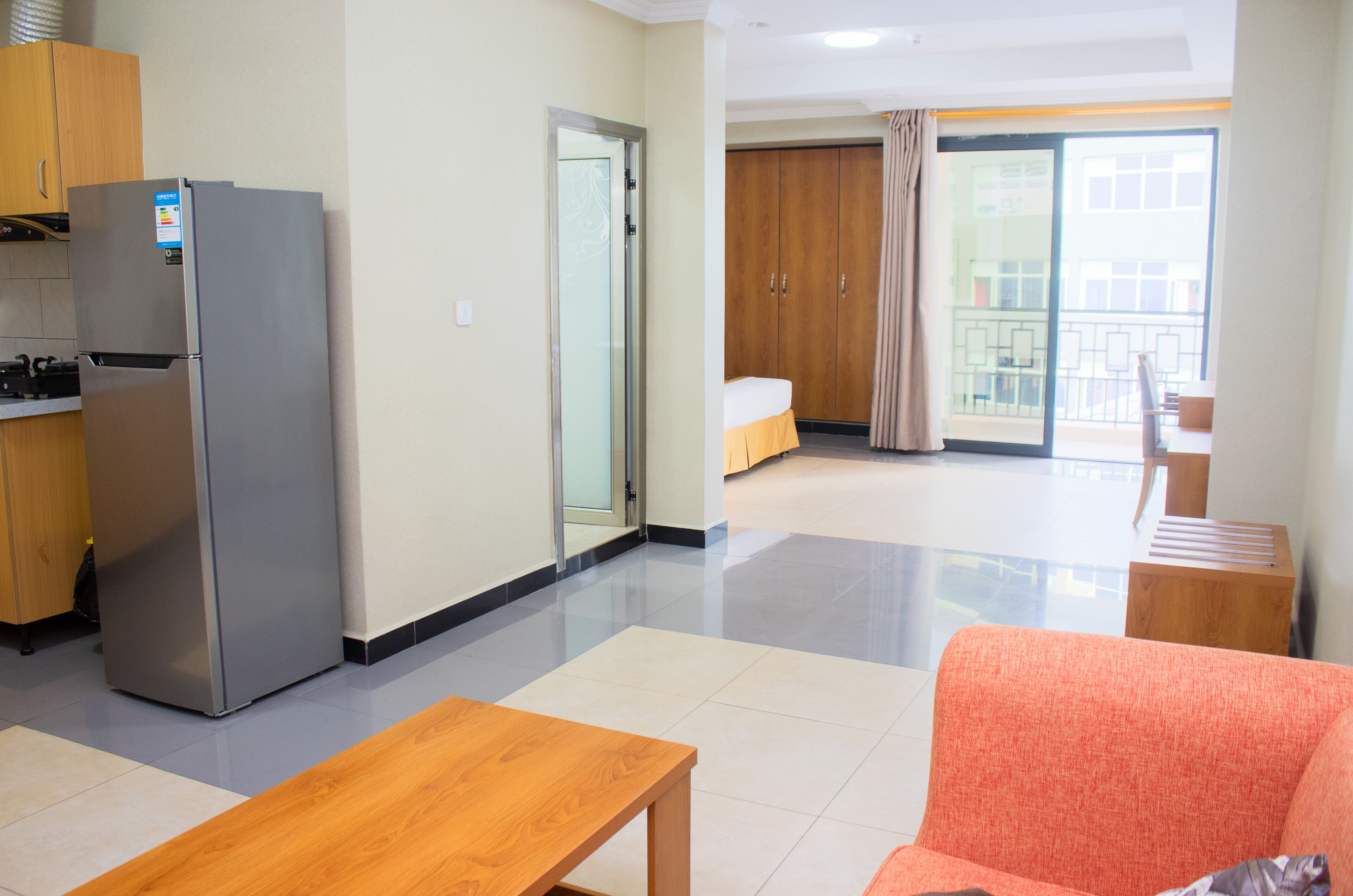 A modern hotel room with a kitchenette, a bed, a balcony, and a seating area.