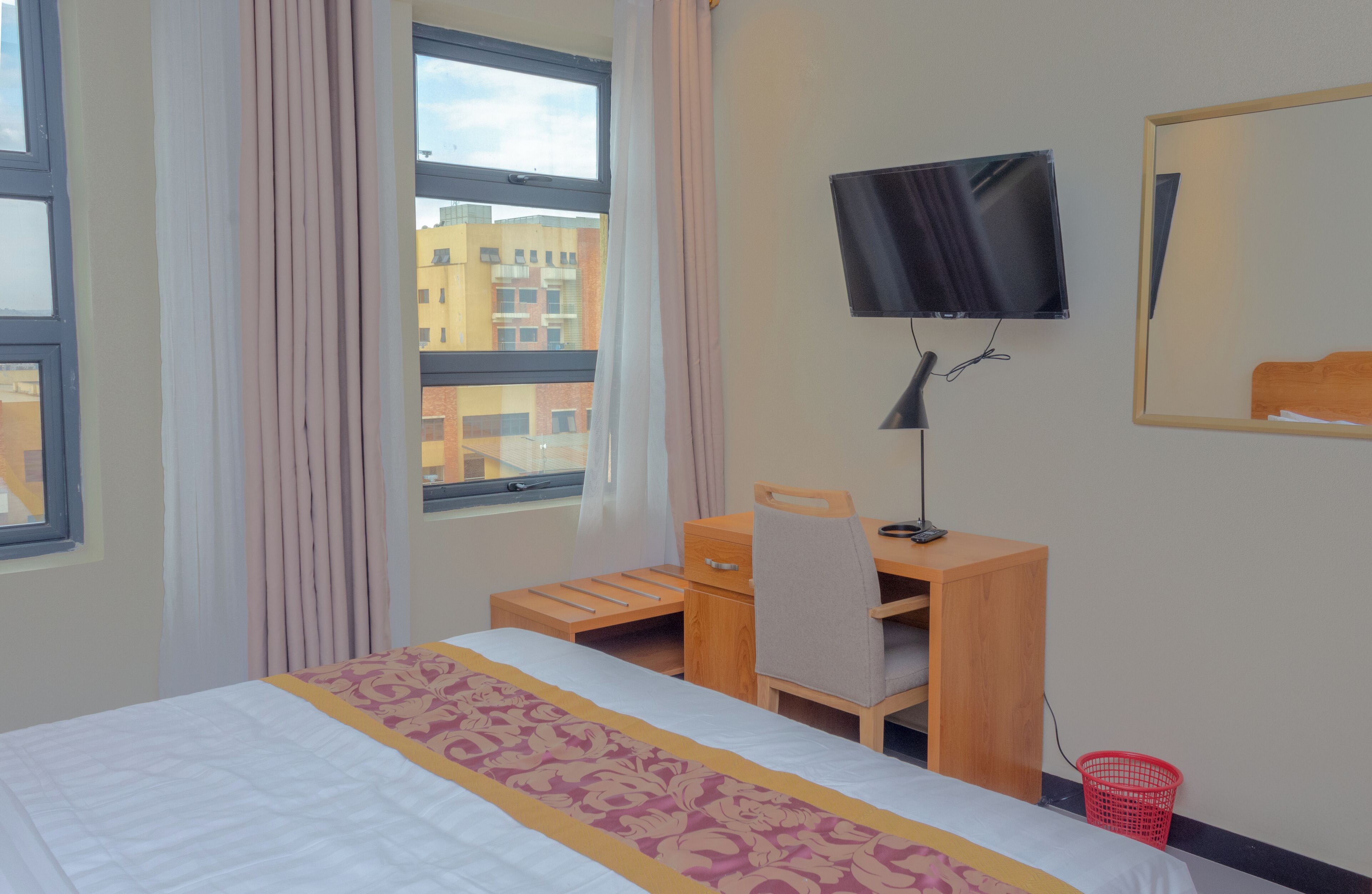 Camera d'albergo con un letto, una scrivania, una sedia, una televisione e una finestra con tende.