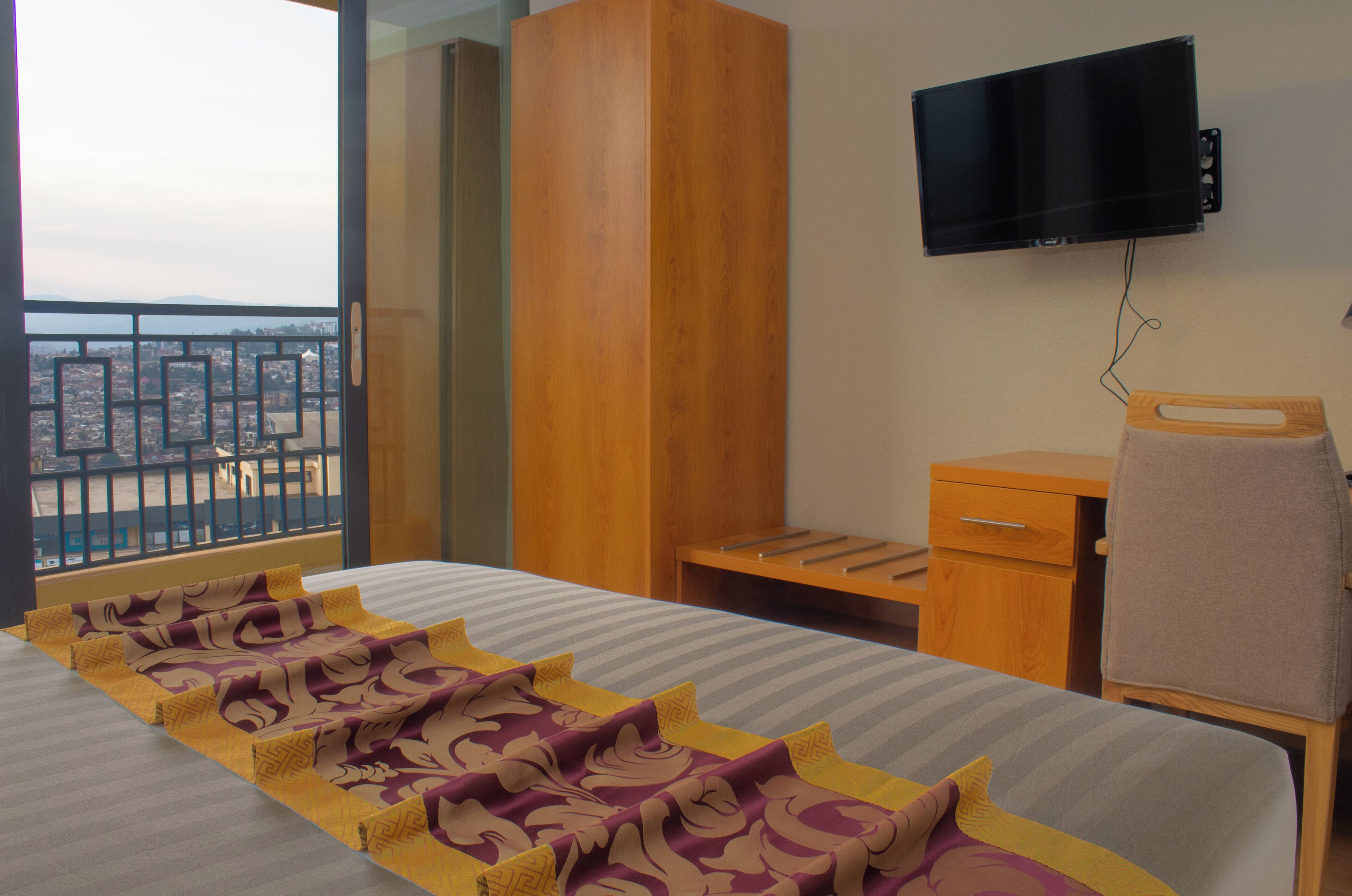 Une chambre d’hôtel comprenant un lit, une armoire en bois, un bureau, une chaise, un téléviseur fixé au mur et un balcon avec une balustrade.