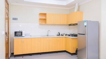 A compact kitchen with wooden cabinets, a stainless steel refrigerator, a microwave, and a sink.