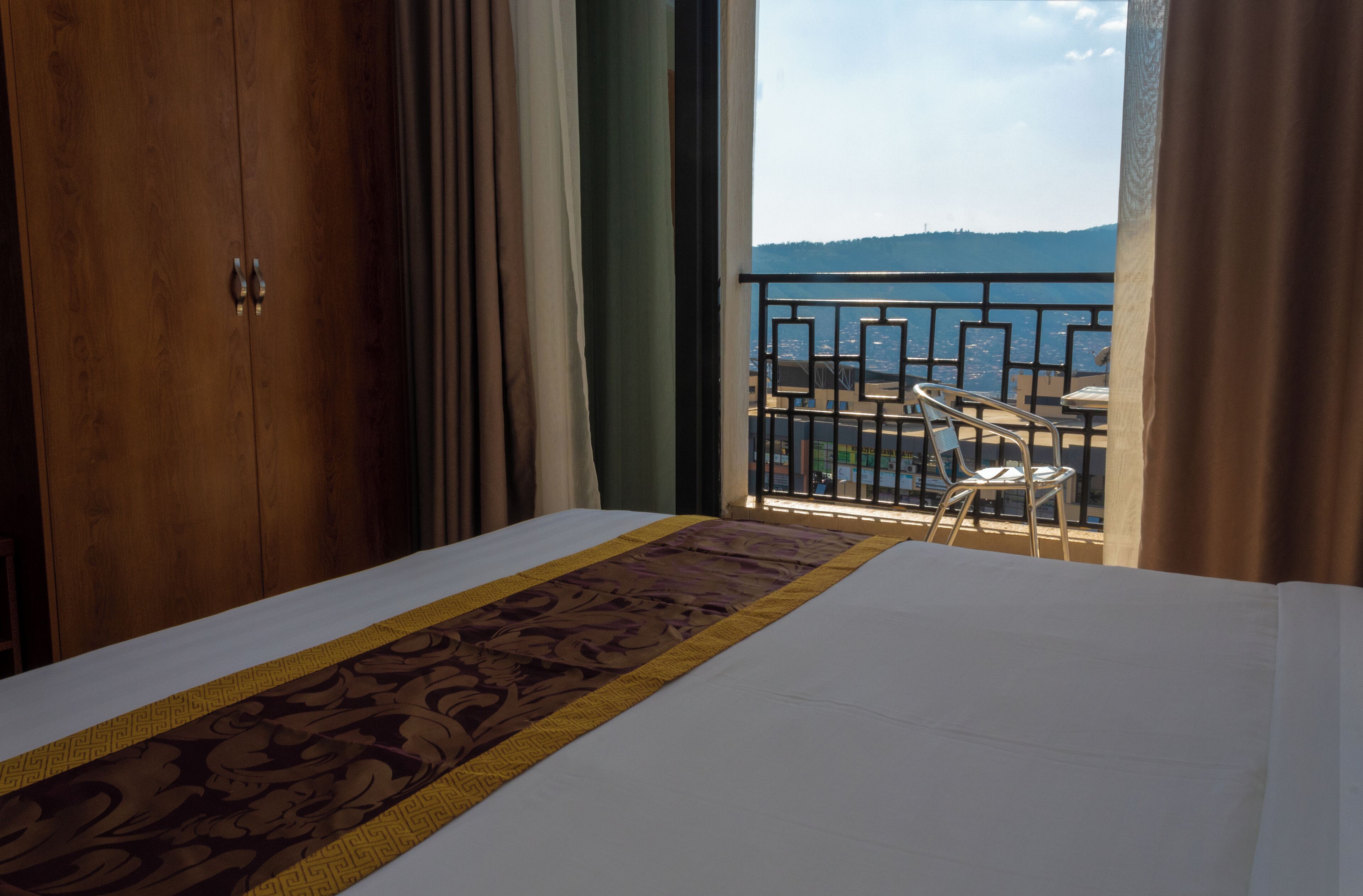 A hotel room with a bed, a balcony with a view of the sea, and a wooden wardrobe.