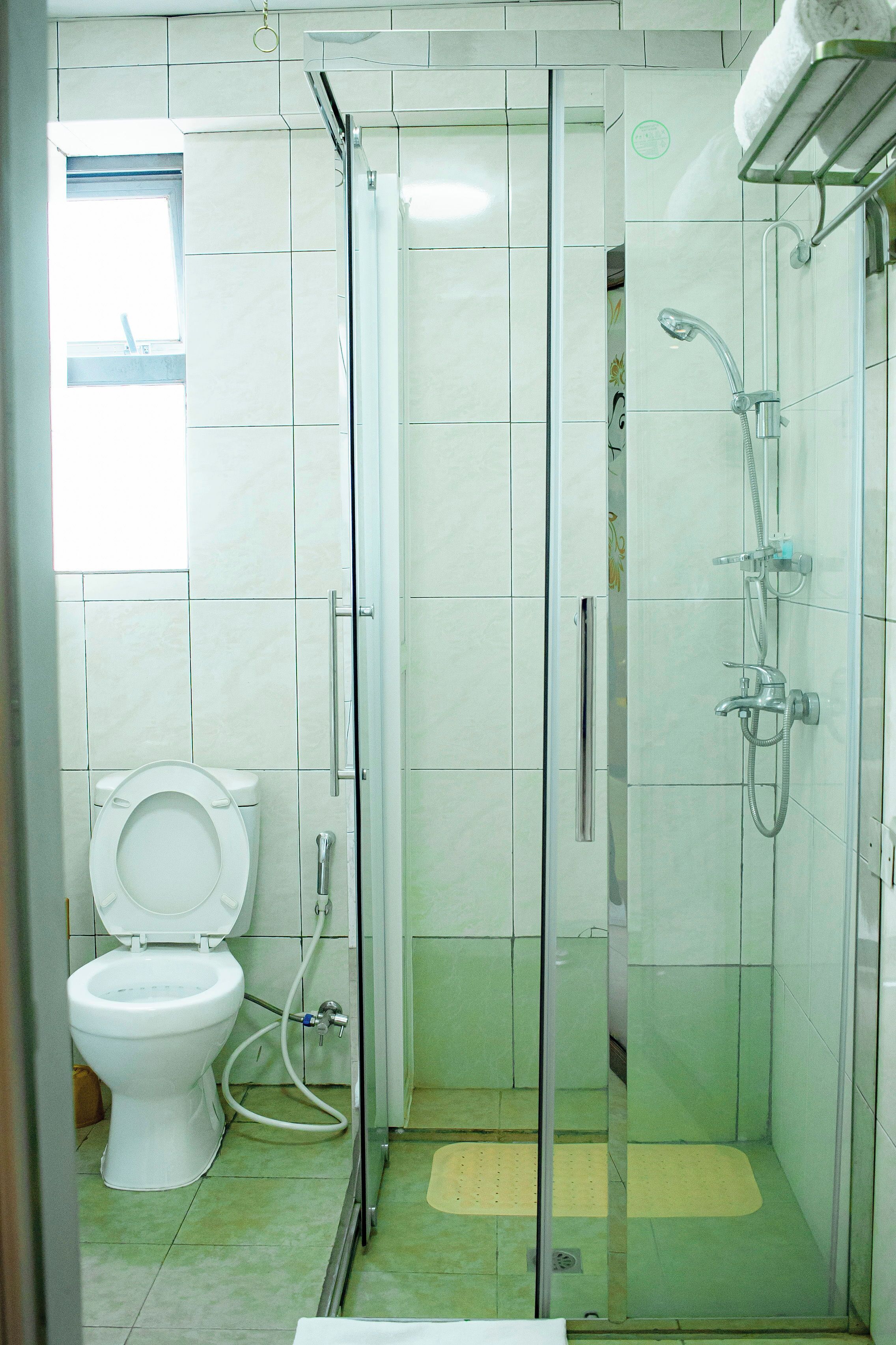 Un baño con inodoro, ducha con puerta de cristal y un ventanal pequeño.