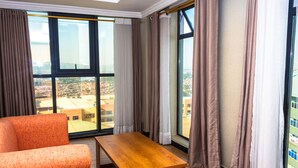 A modern room with a large window, a wooden table, and an orange chair. - Tropical Plaza Apartments (Kigali)