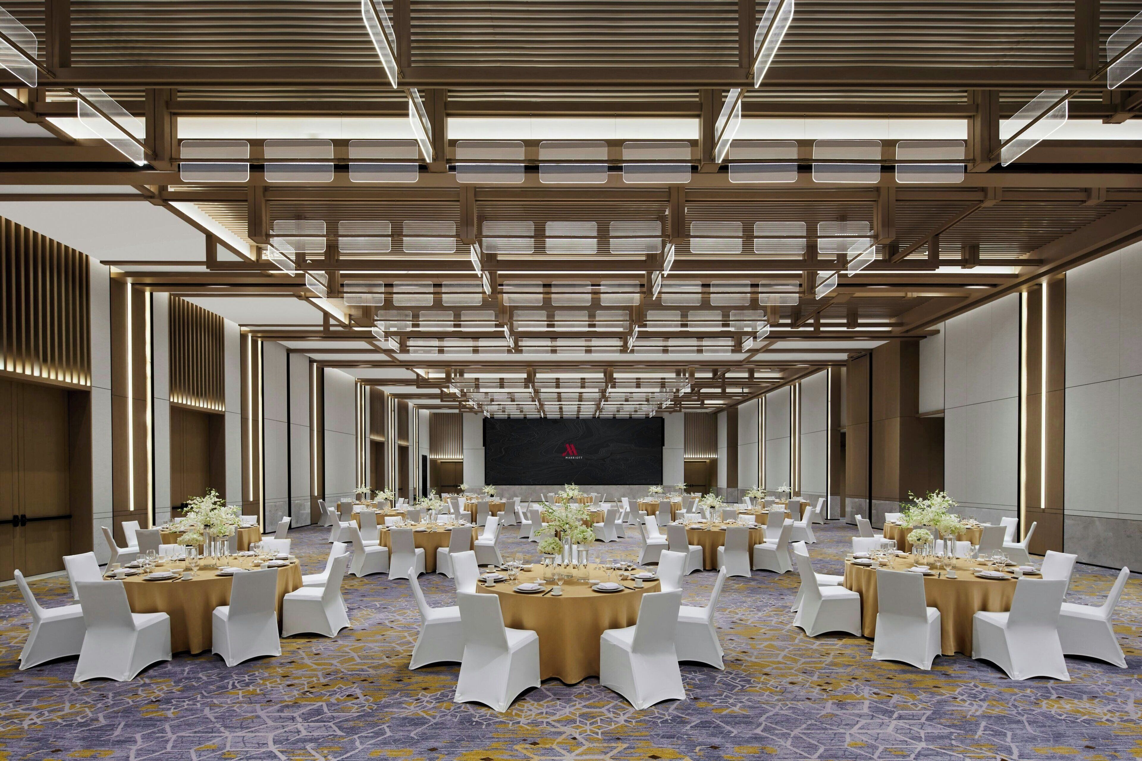A conference room with multiple round tables, white chairs, and a large screen at the front.
