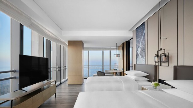 A modern hotel room with a large flat-screen TV, a bed, a sofa, and a dining area with a view of the city. - Changzhou Marriott Hotel Jintan (Changzhou)