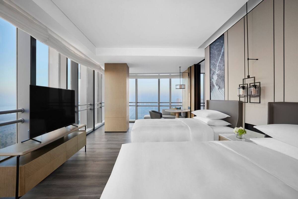 Une chambre d’hôtel moderne dotée d’un grand téléviseur à écran plat, d’un lit, d’un canapé et d’un coin repas offrant une vue sur la ville.