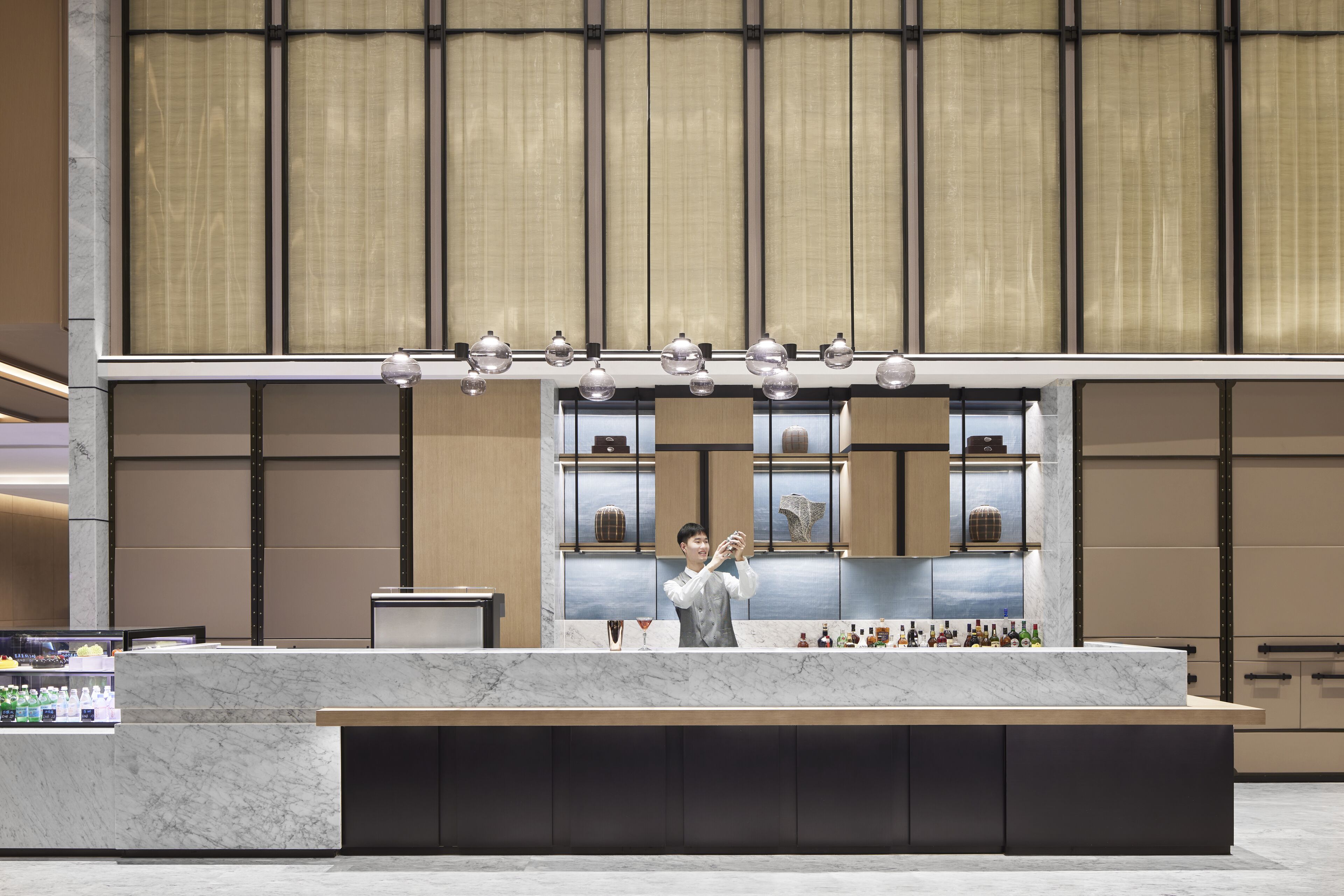 A modern hotel lobby with a marble reception desk, a bar area with bottles, and a large window with curtains.