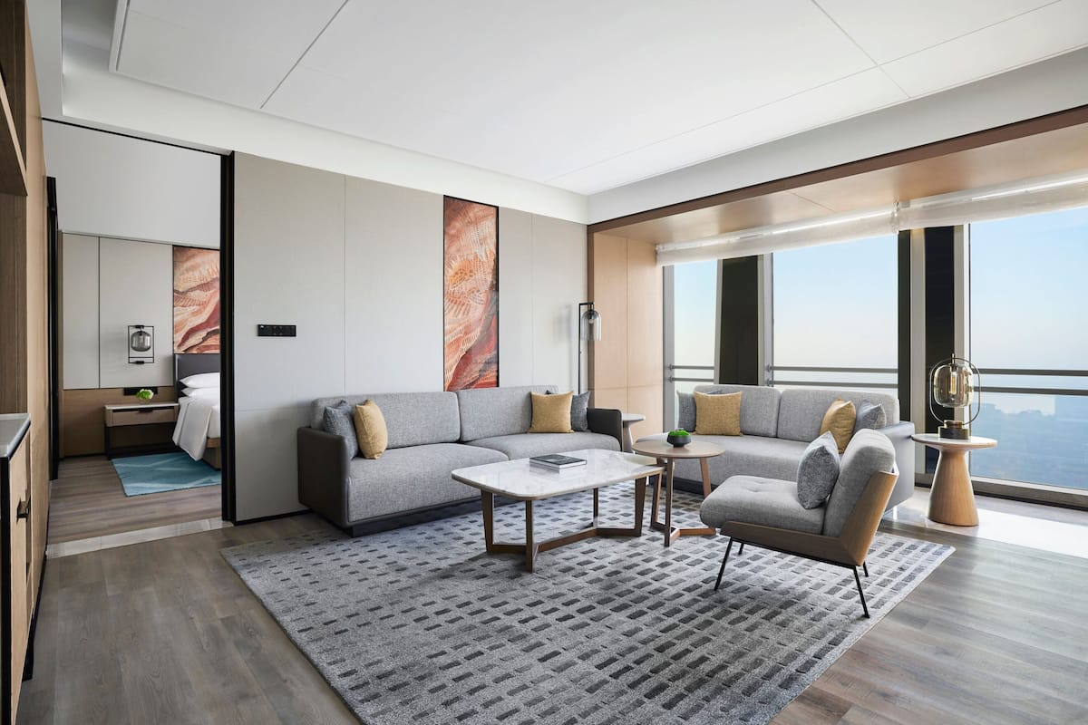 Un salon moderne avec un canapé gris, une table basse et une vue sur la ville grâce à de grandes fenêtres.