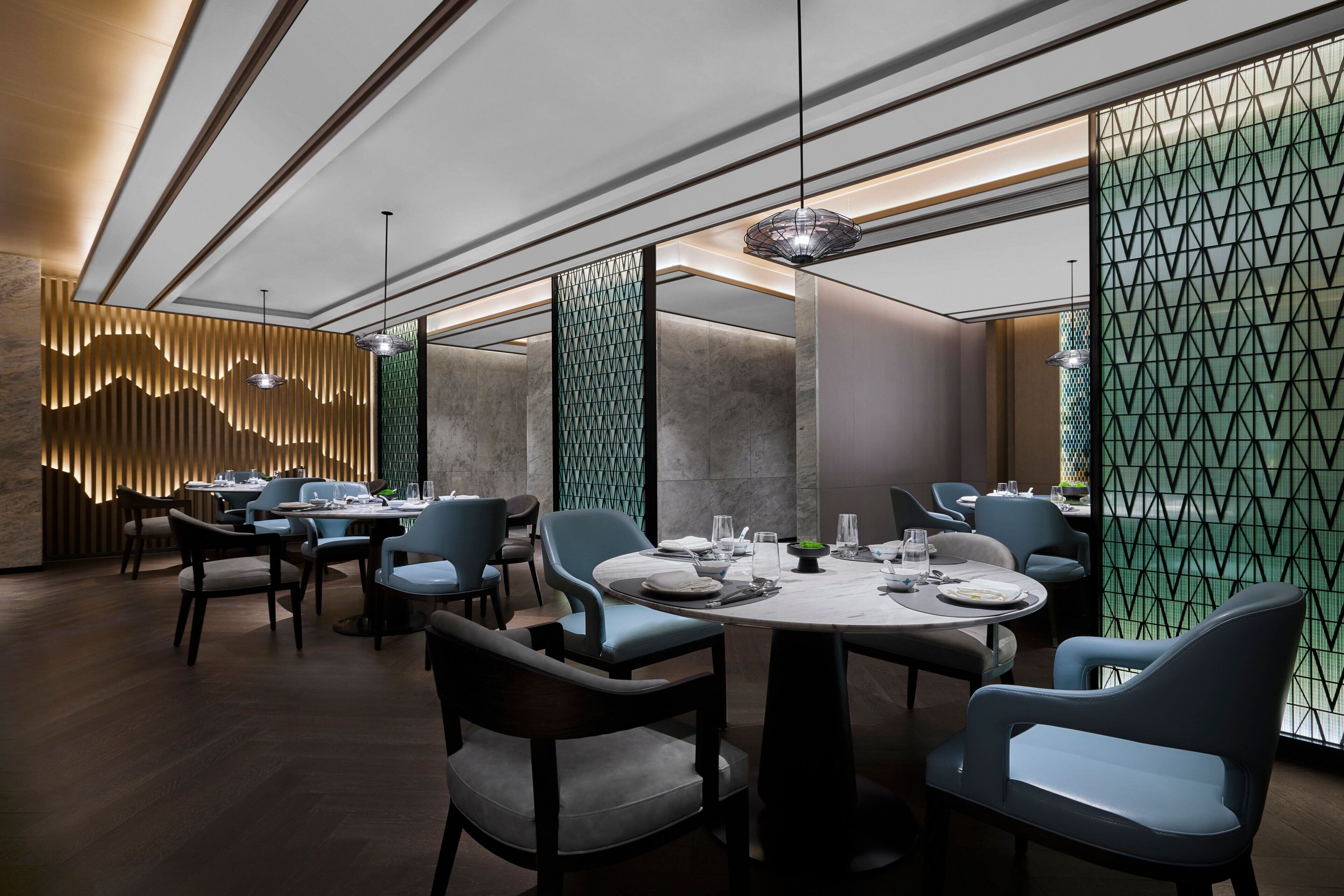 A modern dining area with round tables, blue chairs, and pendant lighting.