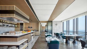 A modern dining area with a long counter, multiple tables, and chairs. - Changzhou Marriott Hotel Jintan (Changzhou)