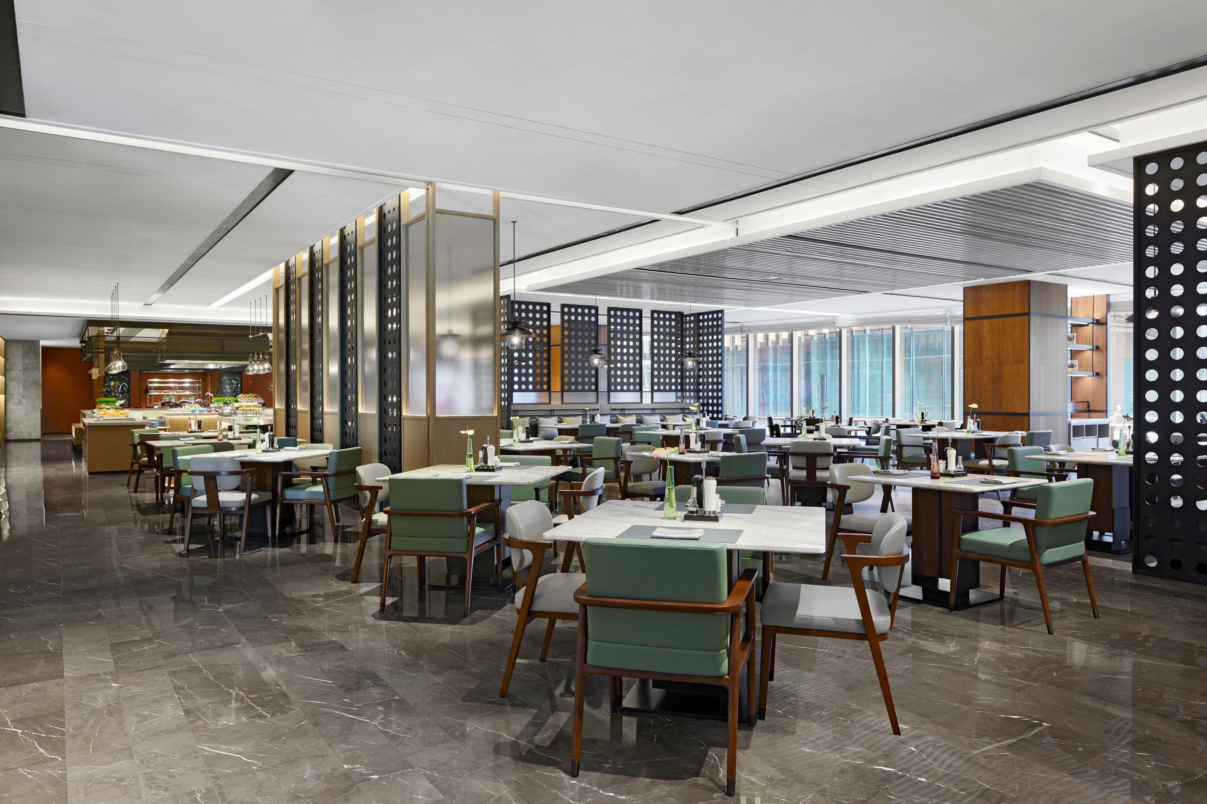A modern dining area with multiple tables and chairs, a kitchen in the background, and a decorative wall with circular cutouts.