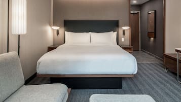 A modern hotel room with a large bed, two bedside tables, a nightstand, a chair, and a bench.