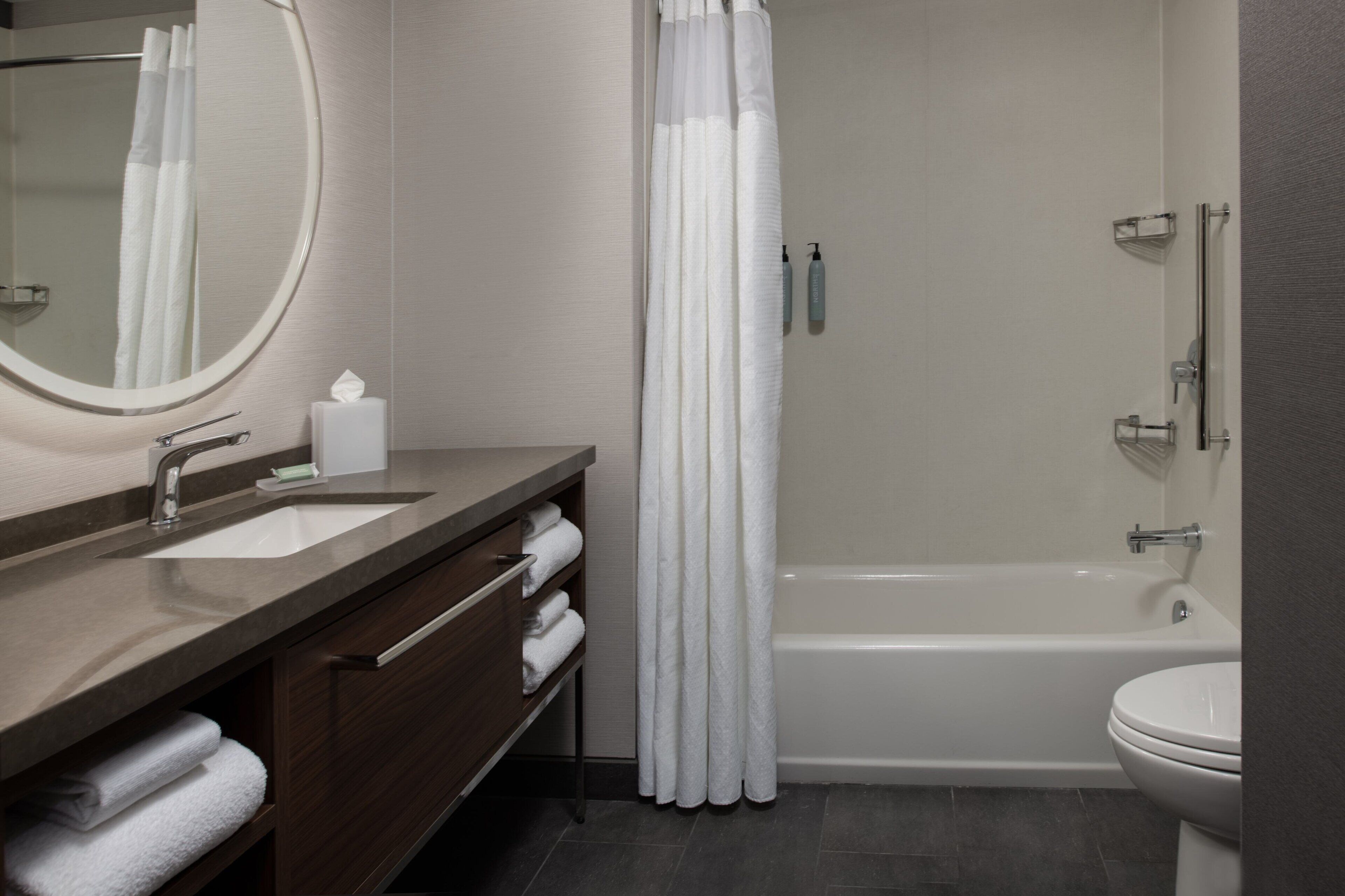 A modern bathroom with a bathtub, a toilet, a sink with a mirror, and a shower curtain.
