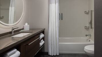 A modern bathroom with a bathtub, a toilet, a sink with a mirror, and a shower curtain.