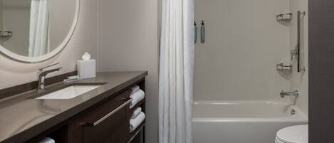 A modern bathroom with a bathtub, a toilet, a sink with a mirror, and a shower curtain.