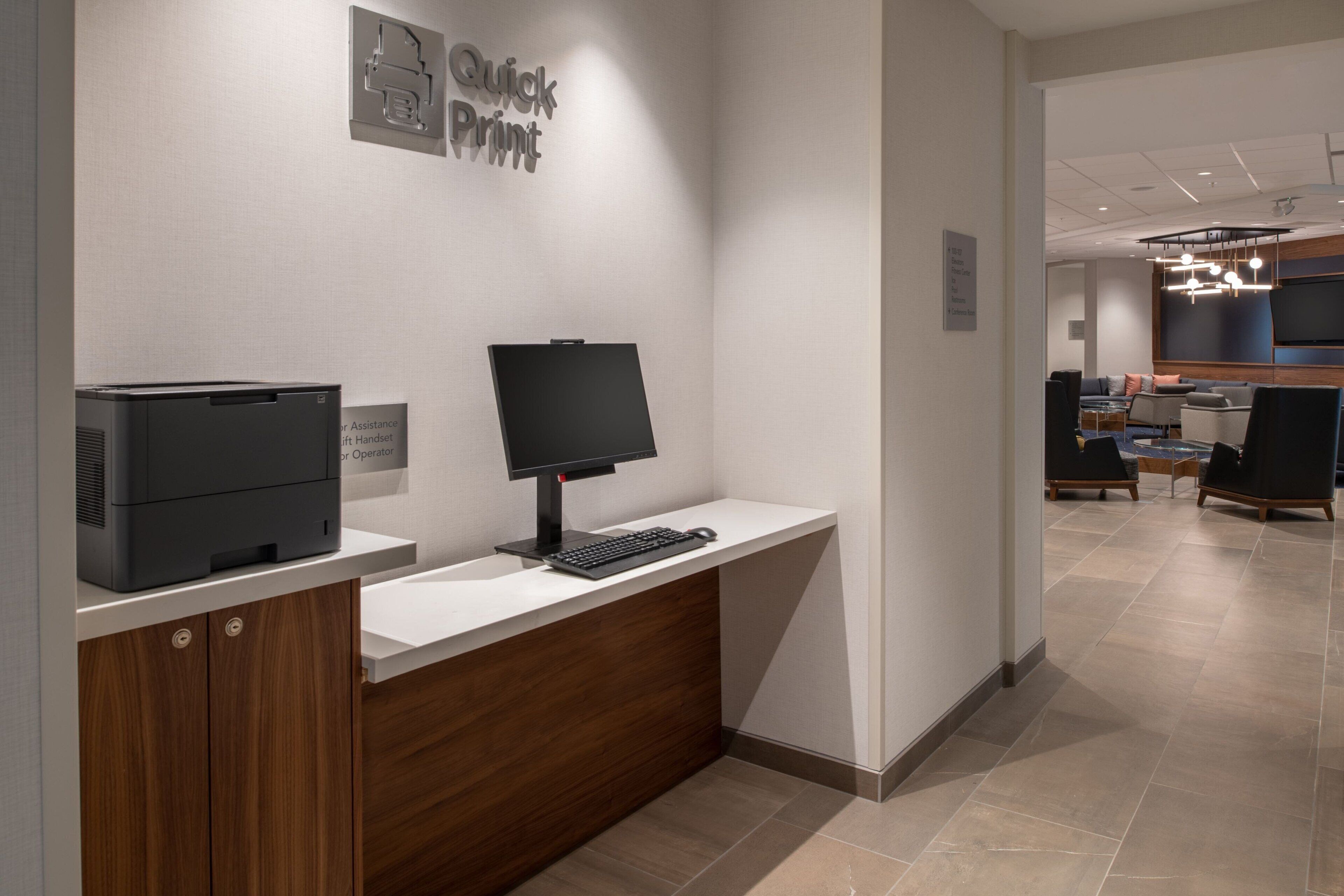 A reception desk with a printer and monitor, a sign for 'Quick Print', and a modern interior with a sofa and TV in the background.