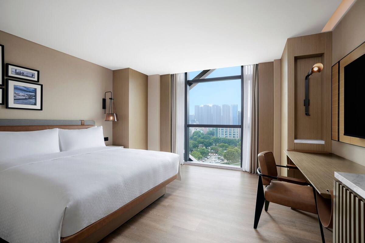 A modern hotel room with a large bed, a desk, and a view of the city.