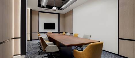 A conference room with a long table, several chairs, and a projector screen.
