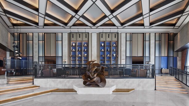 Un hall d’entrée spacieux au design moderne, agrémenté d’une sculpture centrale, d’un escalier et d’un espace détente avec des tables et des chaises.