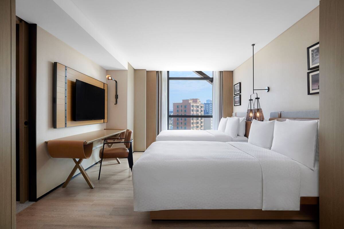 A hotel room with a large bed, a desk with a chair, a TV, and a city view.