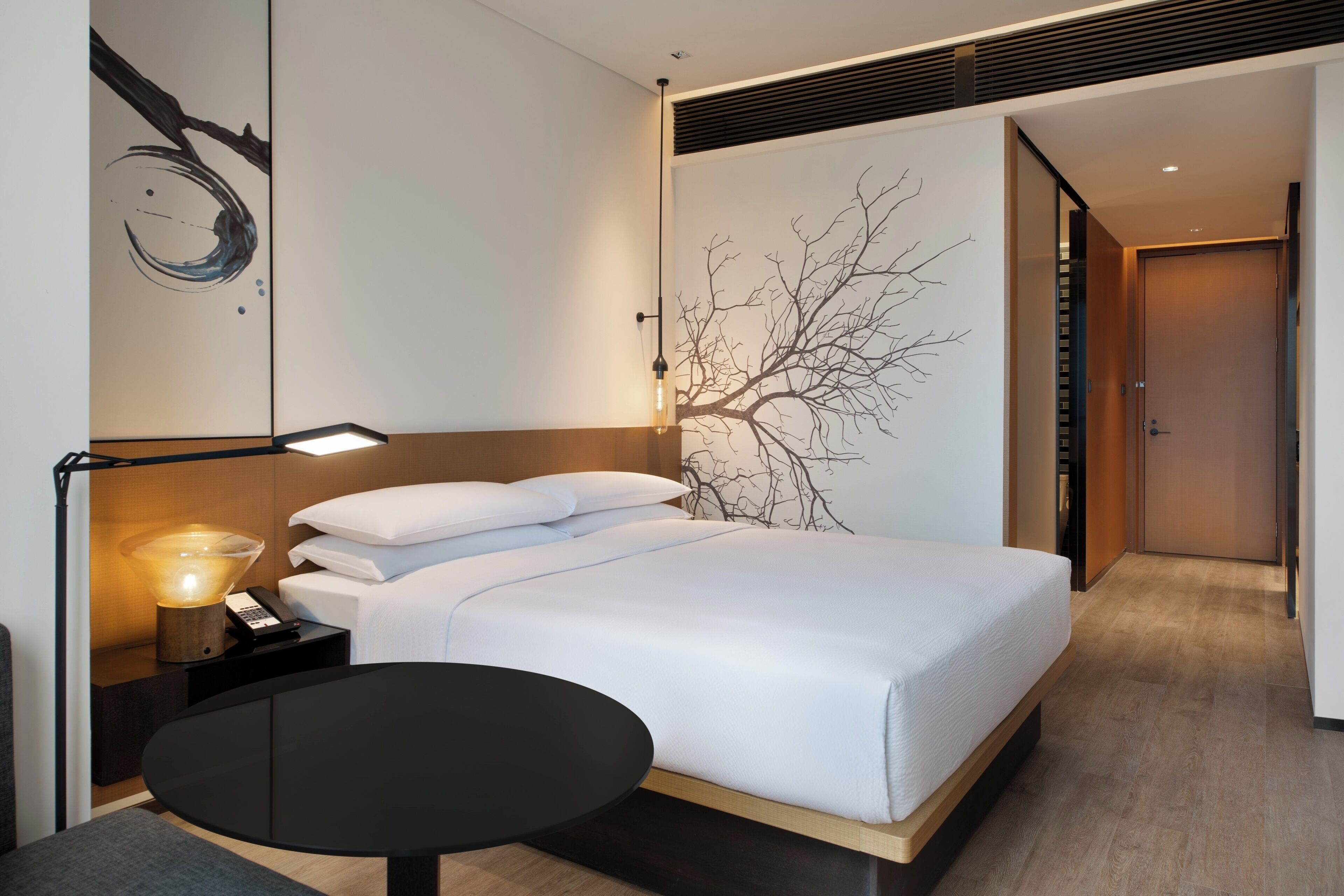 Ett modernt hotellrum med en säng, ett sängbord, en lampa och ett konstverk på väggen.