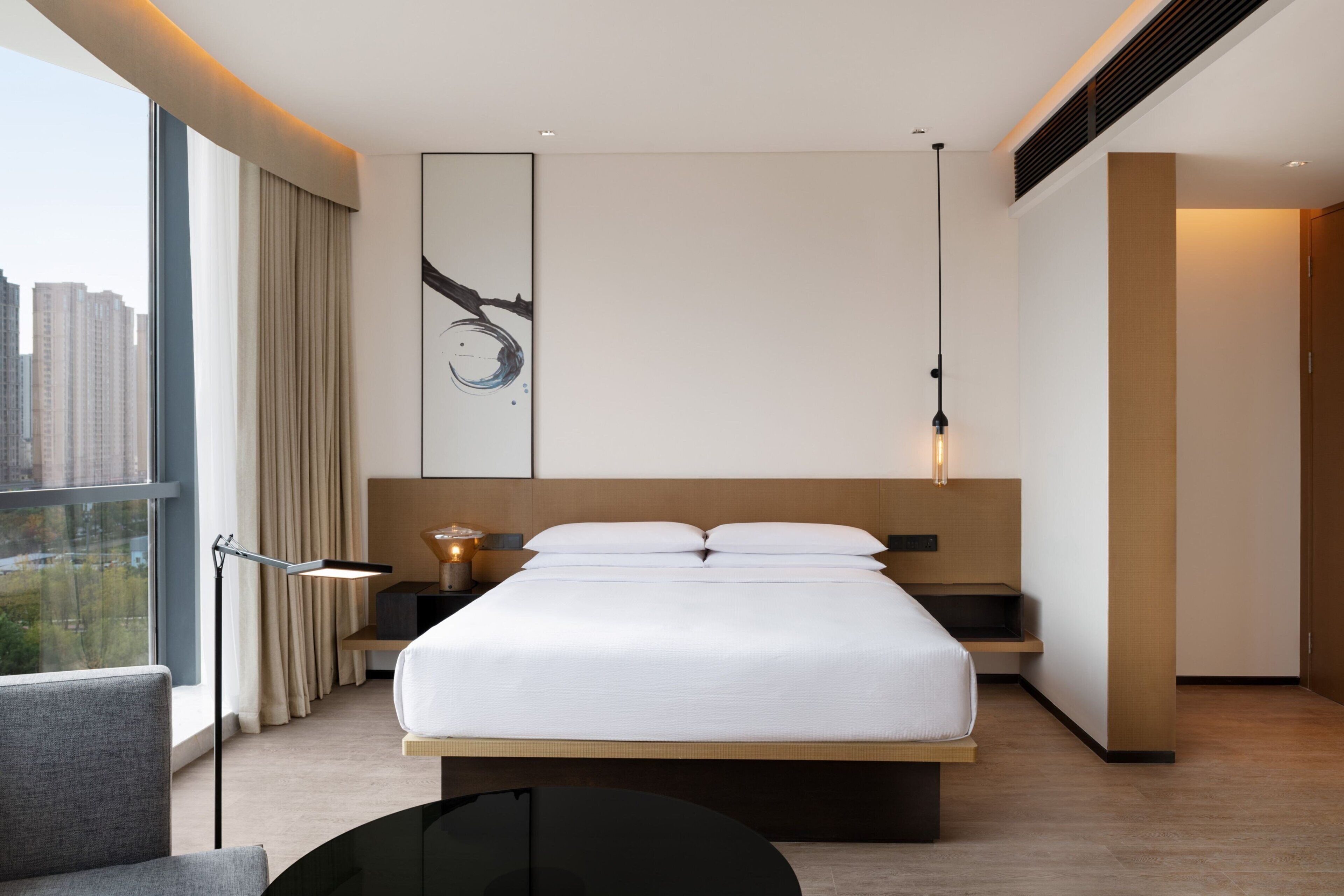 Et moderne hotelværelse med en stor seng, et natbord, et skrivebord og udsigt over byen.