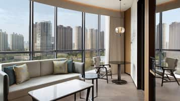 Habitación de hotel moderna con un amplio ventanal que ofrece vistas a la ciudad, un sofá con cojines, una pequeña mesa redonda y una silla.