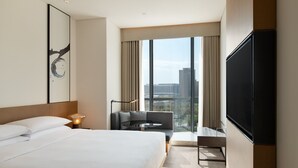 A modern hotel room with a large bed, a flat-screen TV, a sofa, and a city view through large windows. - Fairfield By Marriott Xi'An Chanba (Xi'an)