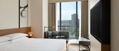 Habitación de hotel moderna con una cama grande, un televisor de pantalla plana, un sofá y vistas a la ciudad a través de amplias ventanas.