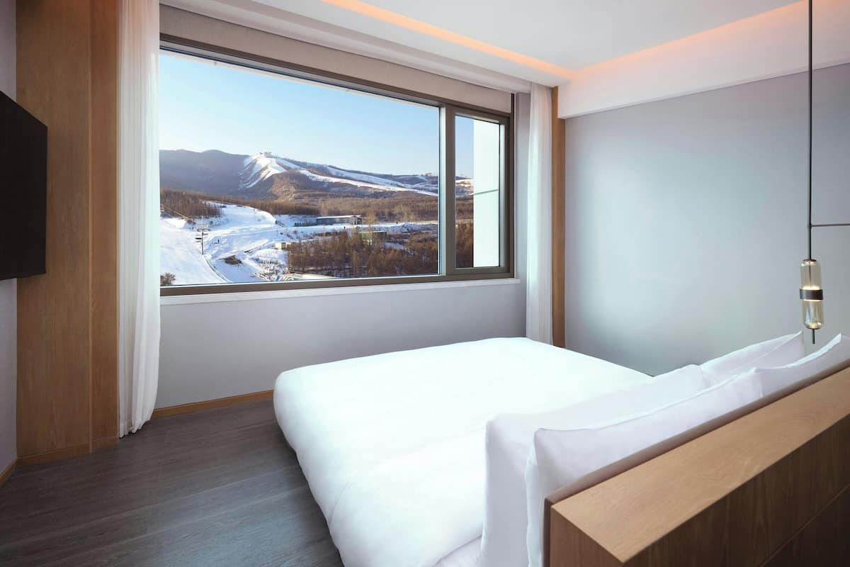 A hotel room with a large window offering a view of a snowy landscape and mountains.