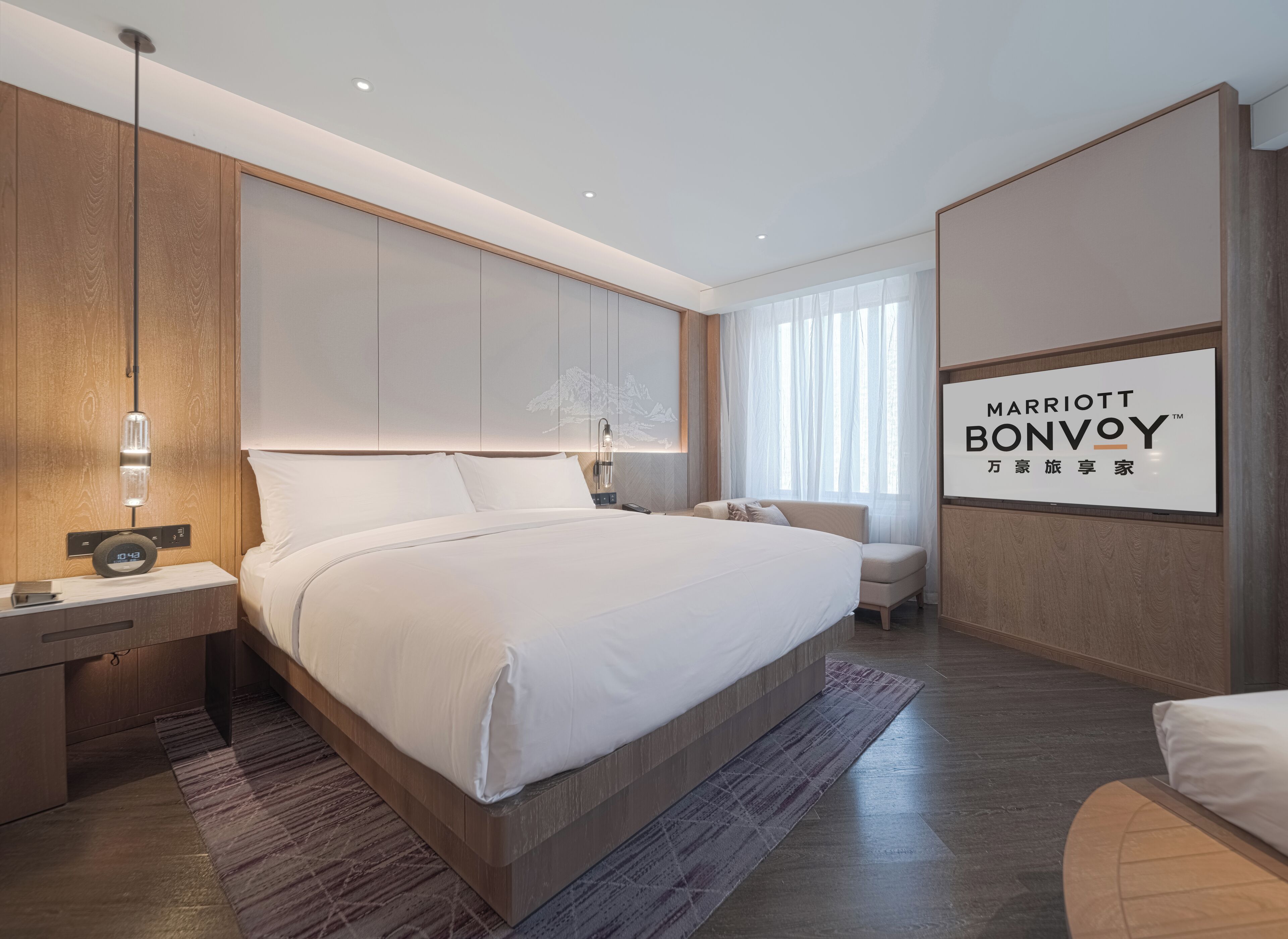 A modern hotel room with a large bed, bedside tables, a desk, and a seating area.