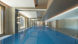 A long, narrow indoor swimming pool with clear blue water, large windows on one side, and a modern architectural design.