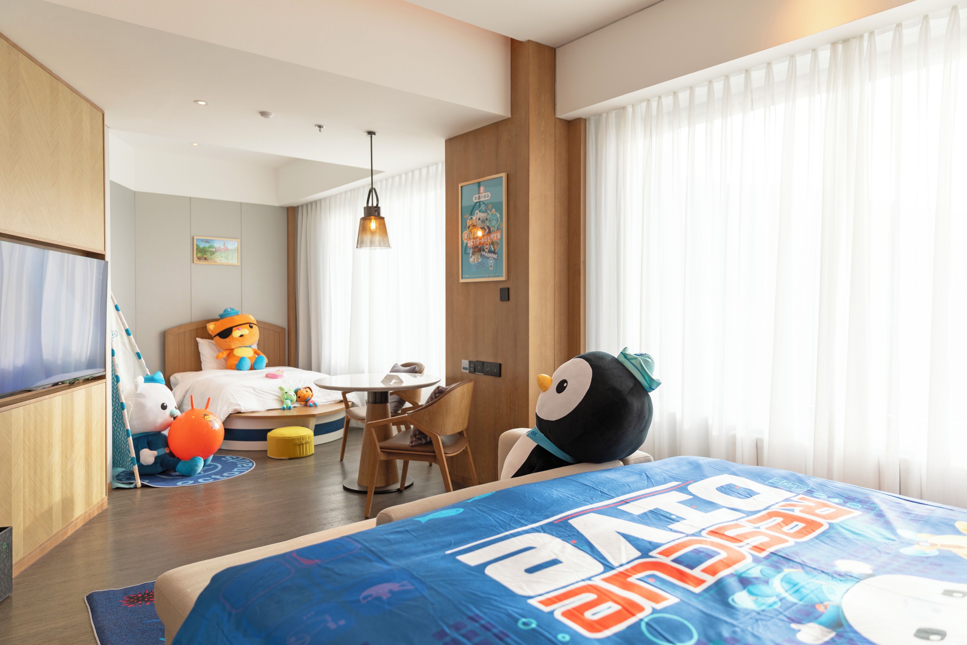A hotel room with a bed, a desk, a chair, a table, and a plush toy.