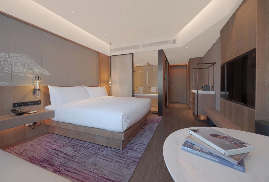 A modern hotel room with a large bed, bedside table, and a TV.