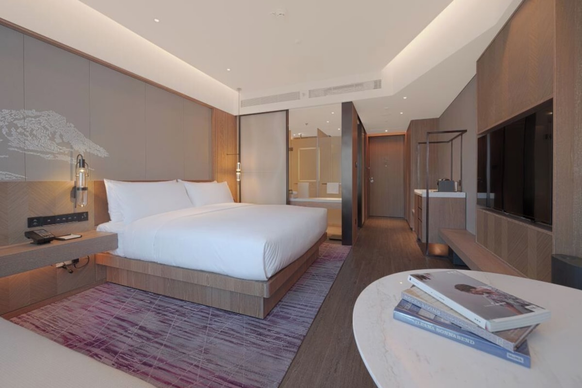 A modern hotel room with a large bed, bedside table, and a TV.