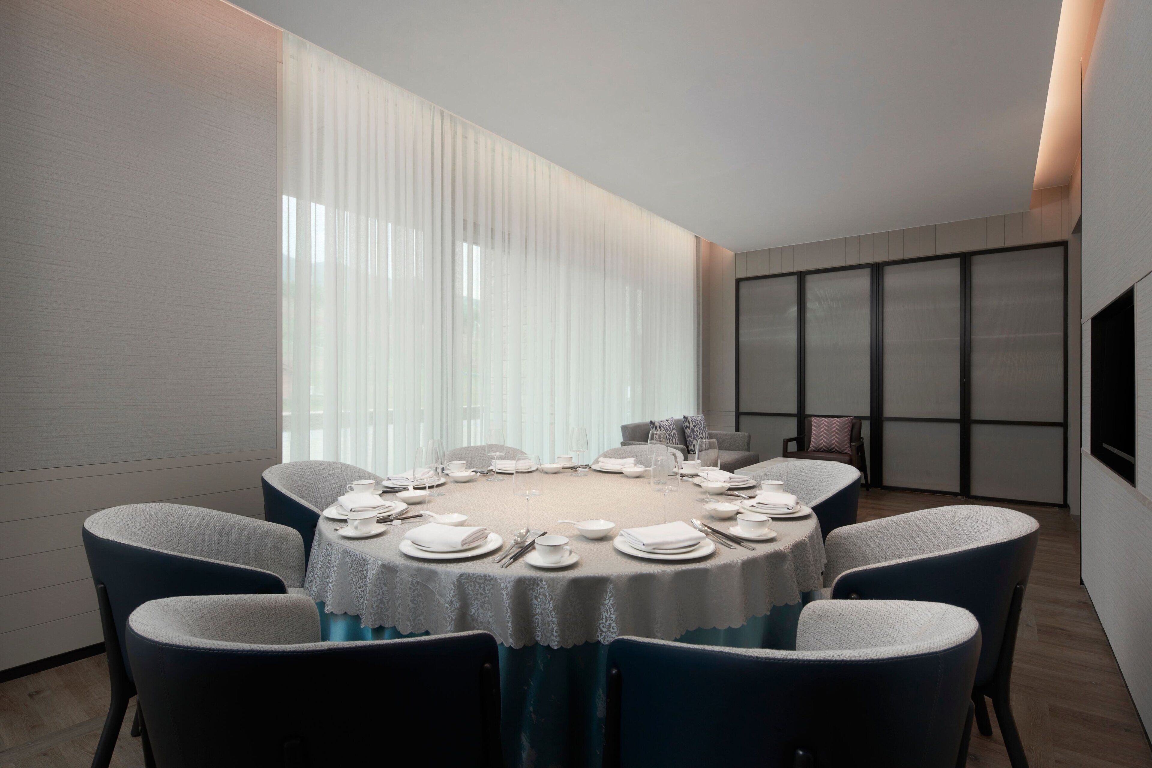 A modern dining room with a round table set for six, surrounded by dark blue chairs.