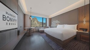 A modern hotel room with a large bed, a desk, and a view of the mountains.