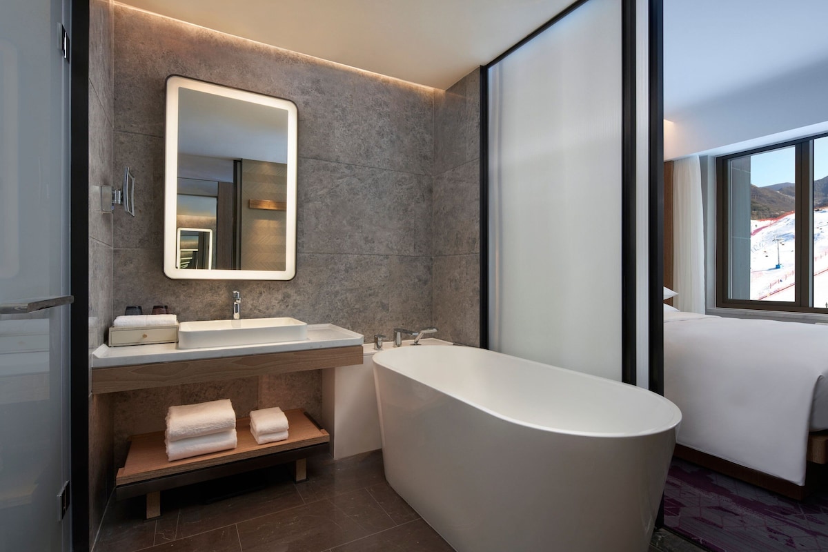 A modern bathroom with a large bathtub, a vanity with a mirror, and a window offering a view of the outdoors.