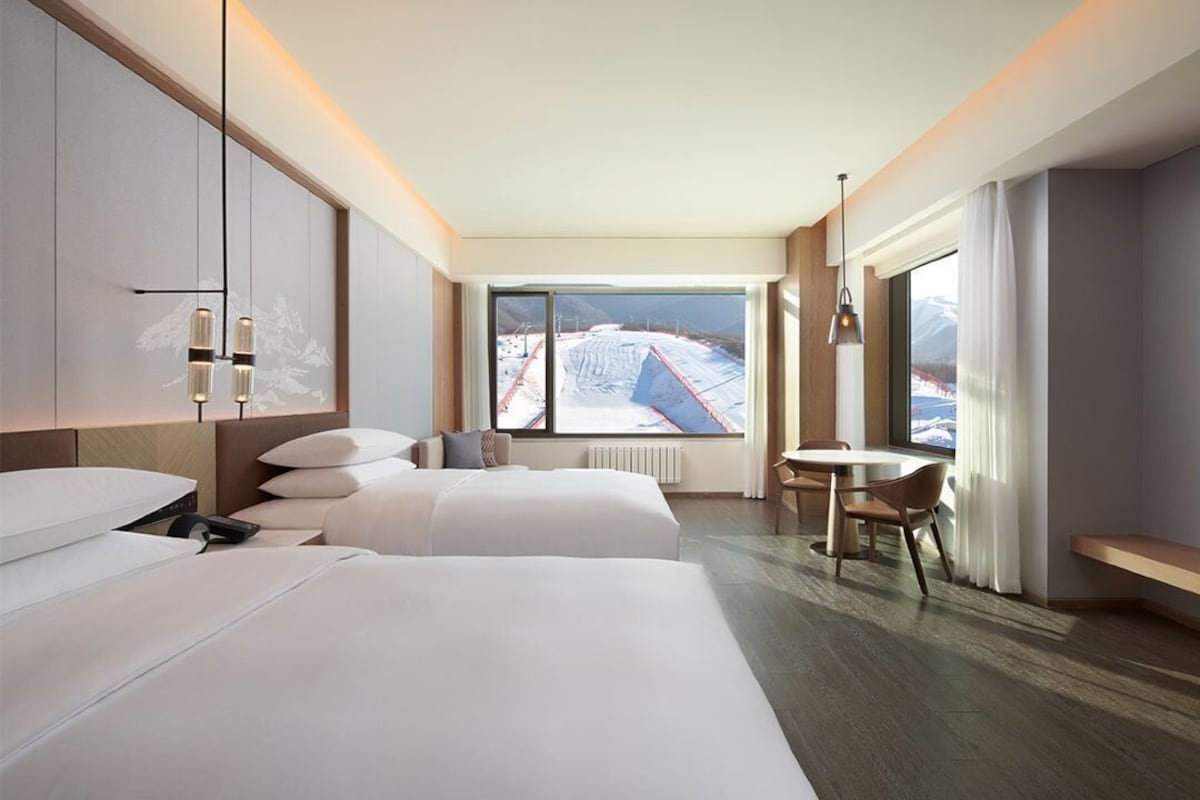 A hotel room with two beds, a dining table, and a view of a snowy landscape.