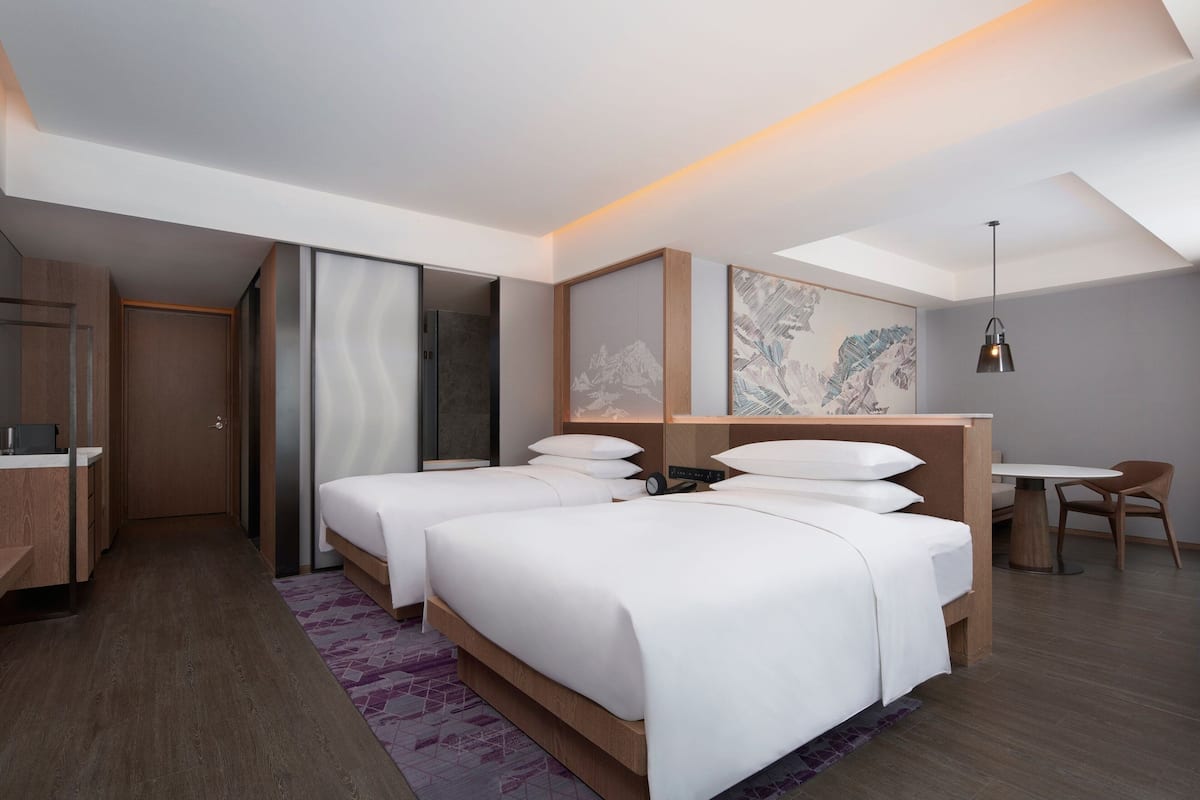 A modern hotel room with two beds, a desk, and a chair.
