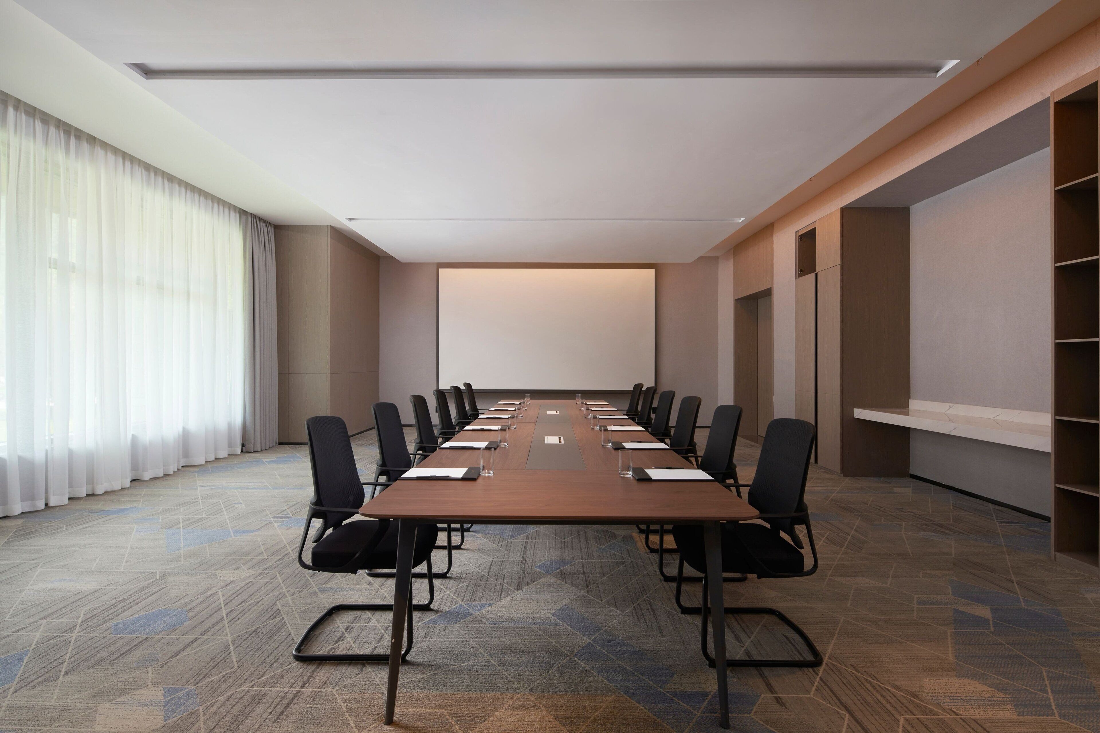 Un salón de conferencias con una mesa larga, sillas y una pantalla para proyector.