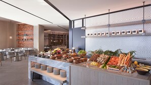 Un área de bufé con diferentes opciones de comida, un espacio de descanso con mesas y sillas, y una cocina al fondo.