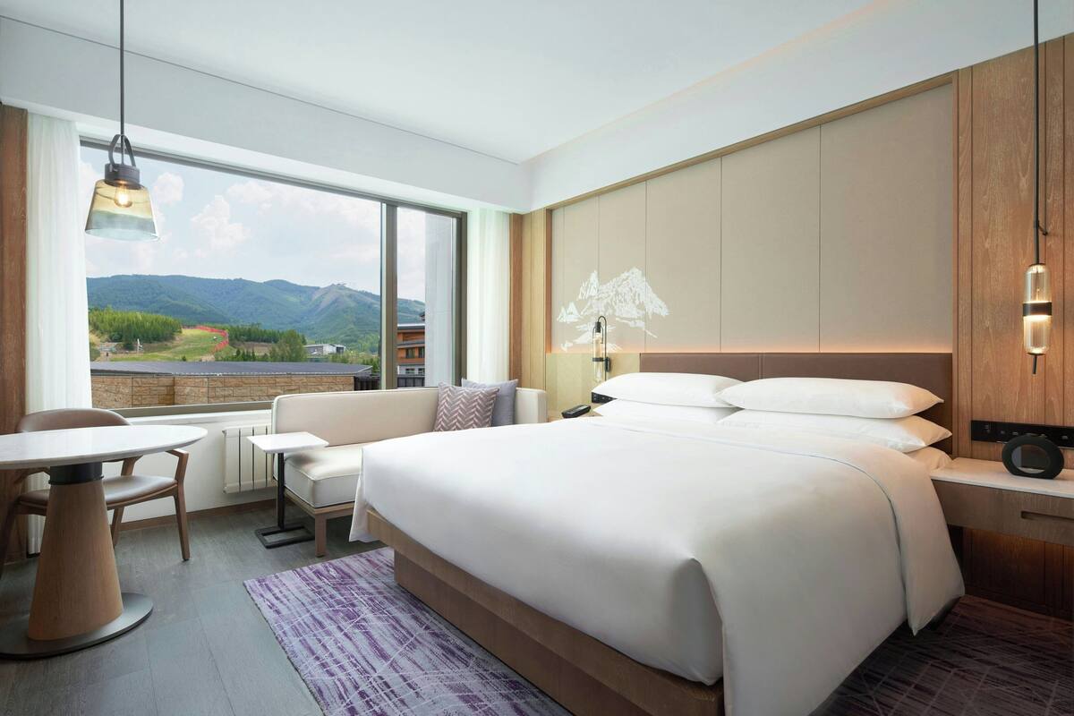 A hotel room with a large bed, a dining table, a sofa, and a view of mountains.