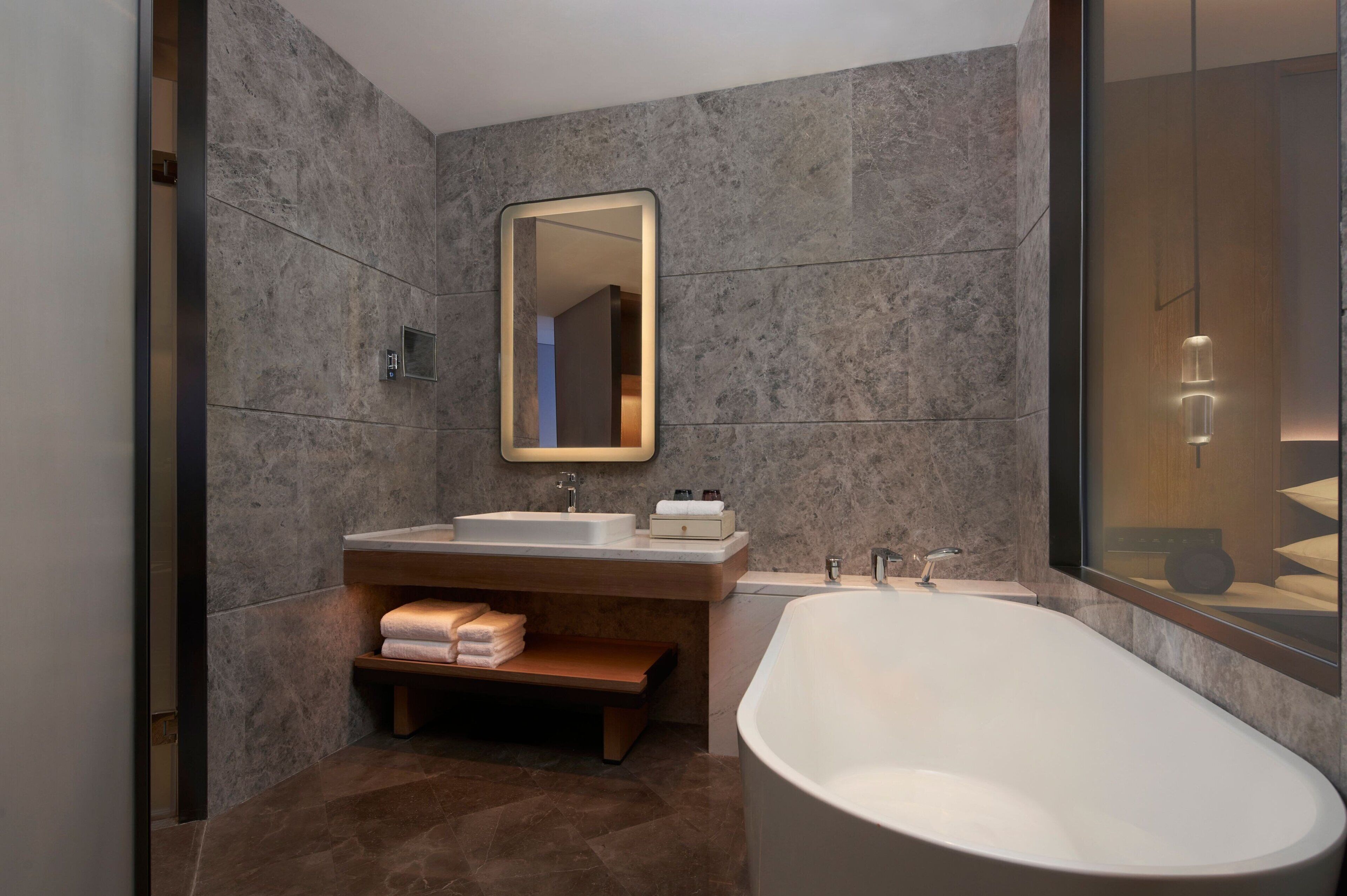 A modern bathroom with a freestanding bathtub, a large mirror, and a vanity with a shelf for towels.