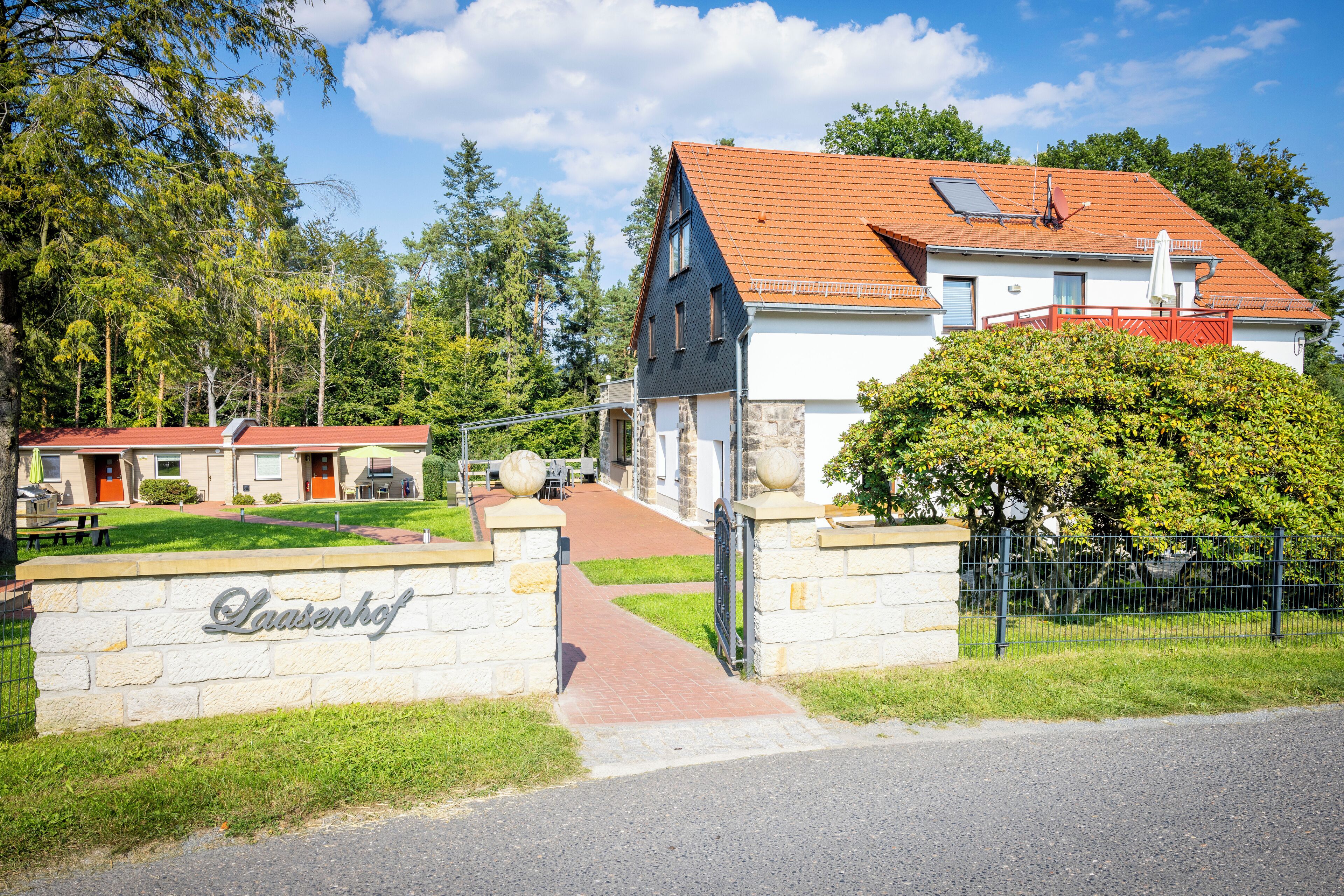 Une maison à deux étages, avec un toit recouvert de tuiles rouges, un portail d’entrée en pierre et une enseigne indiquant « Laasenkof ».