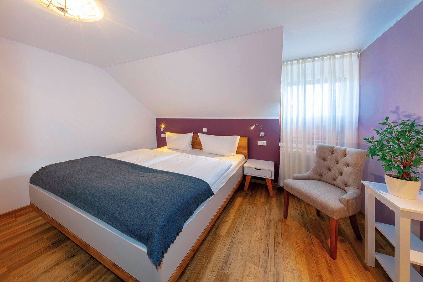 Ein modernes Hotelzimmer mit einem großen Bett, einem Nachttisch, einem Sessel und einer Zimmerpflanze.