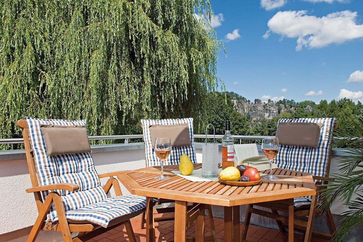 Une terrasse avec deux chaises à rayures, une table en bois et une vue sur le paysage urbain et la verdure.